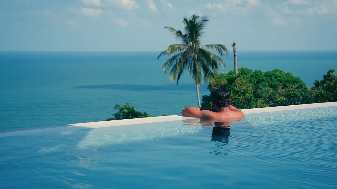 A person at an infinity pool looking out over a calm tropical ocean
