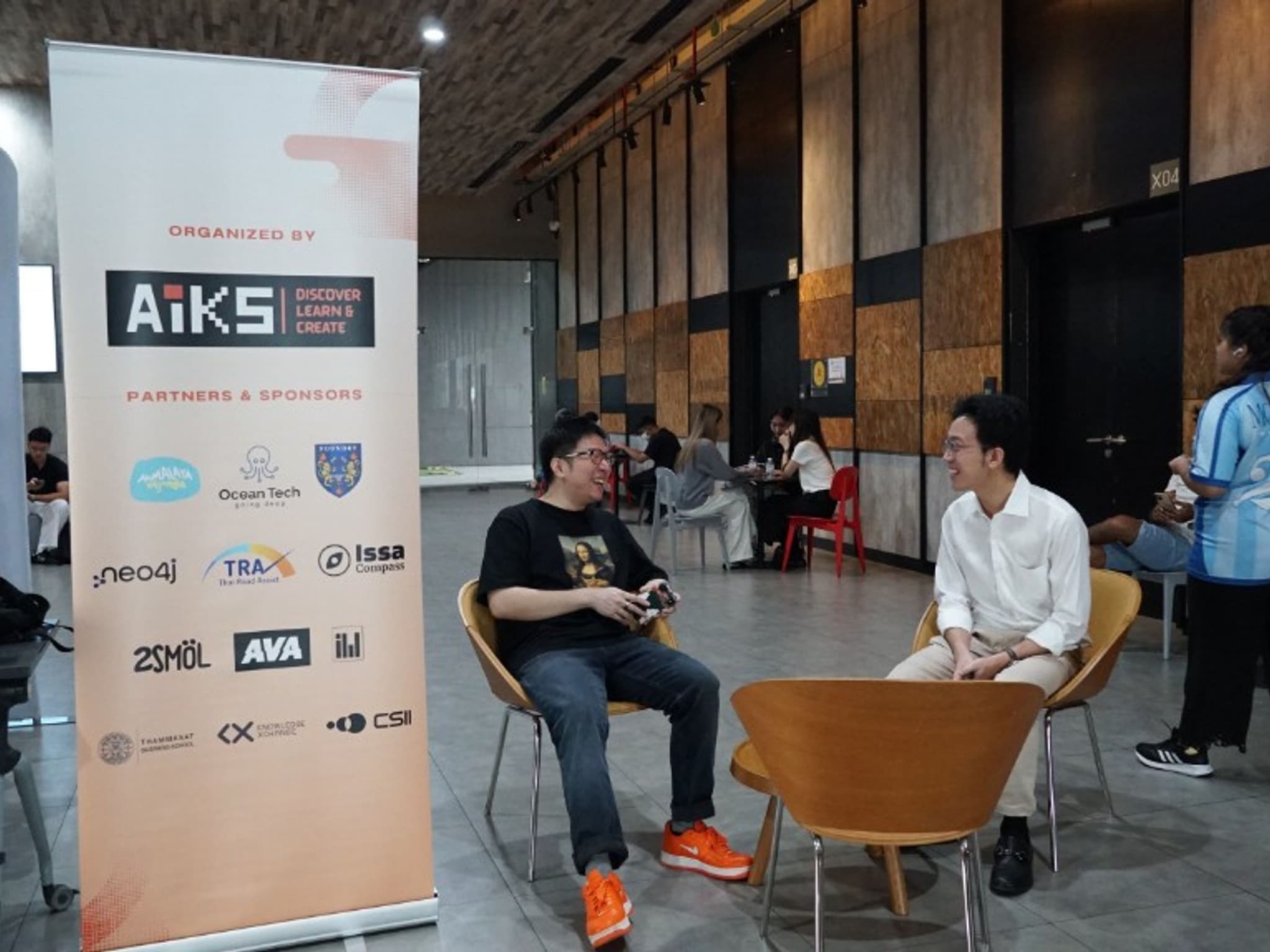 Students and founders talking beside the AIKS partners and sponsors banner listing Issa Compass at KX Knowledge Xchange