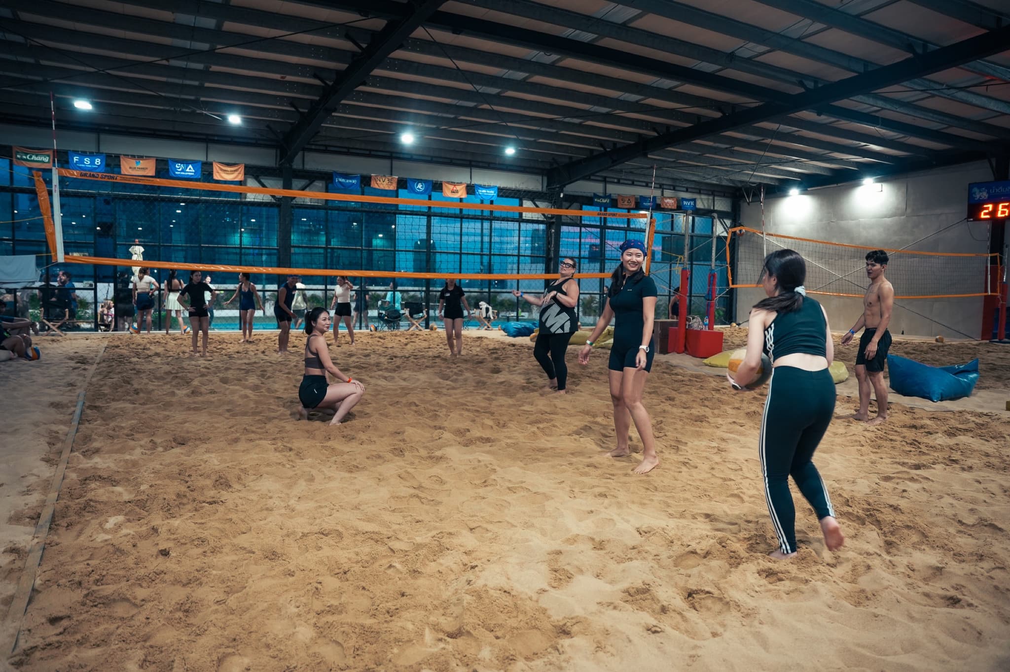 Wide view of the indoor sand volleyball court with players spread across the sand