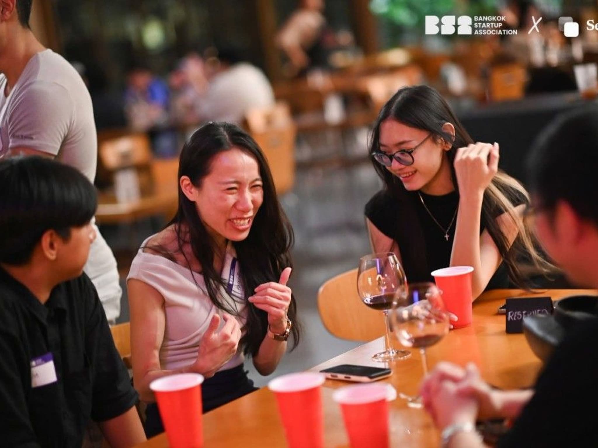 Priscilla Yeung laughing with fellow attendees at a table during the Bangkok Startup Association NØTWORKING Night at Vinyl & Wine, Emsphere