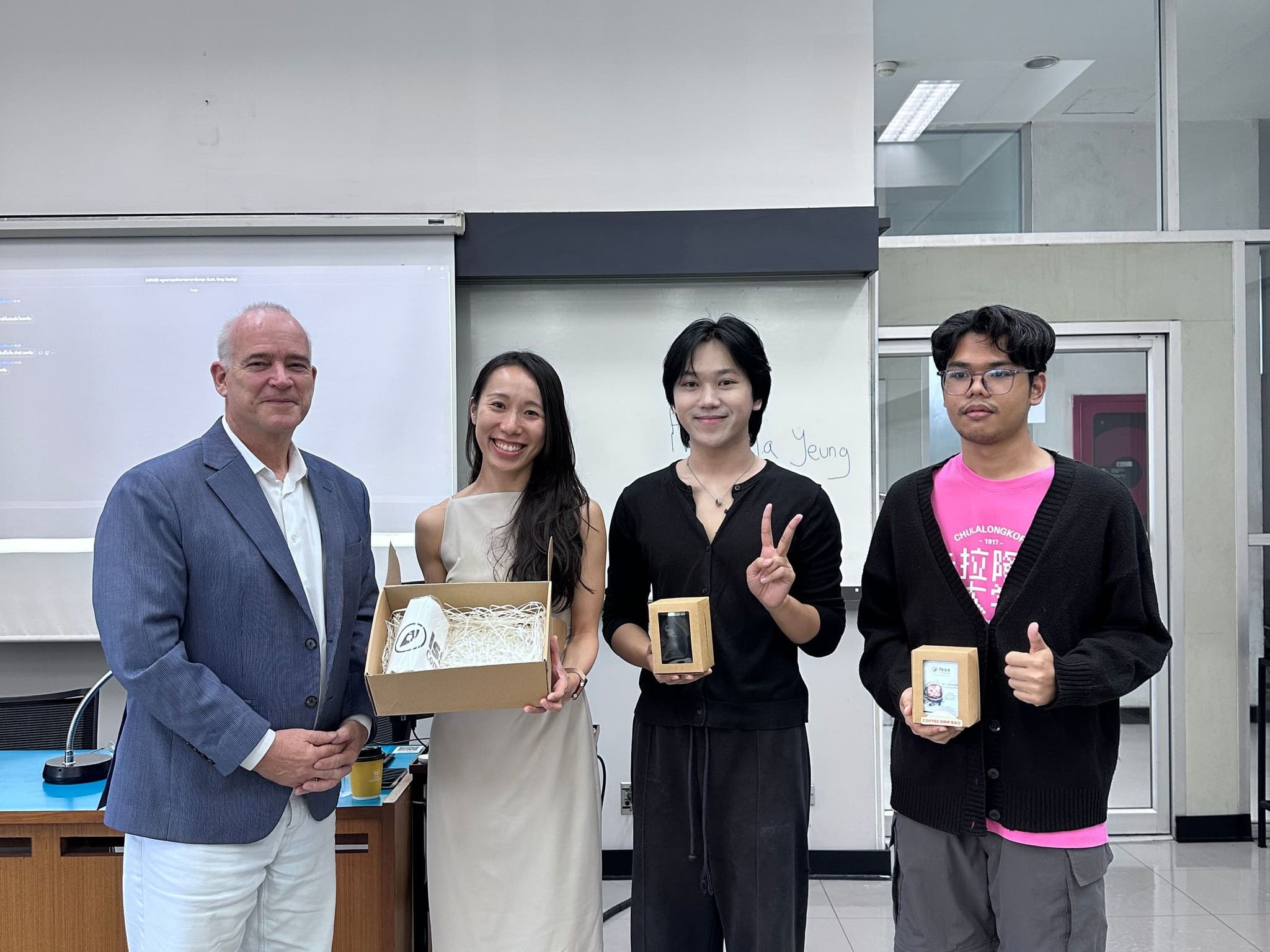 Greg Beatty and Priscilla Yeung with two Chulalongkorn University law students holding small Issa Compass gift boxes at the front of the classroom