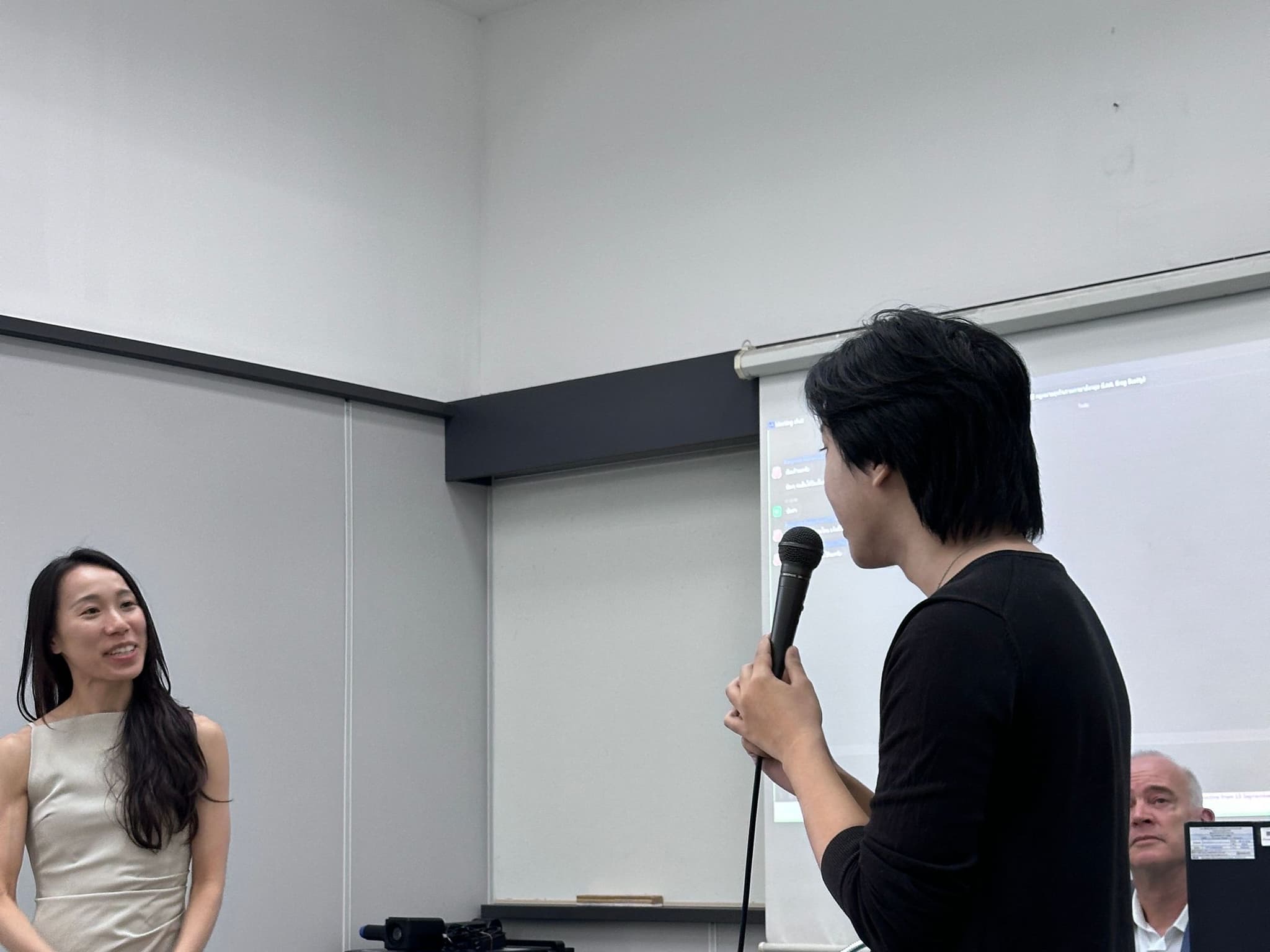 A Chulalongkorn University law student asking Priscilla Yeung a question on the microphone during the Q&A, with Greg Beatty seated at the front of the classroom
