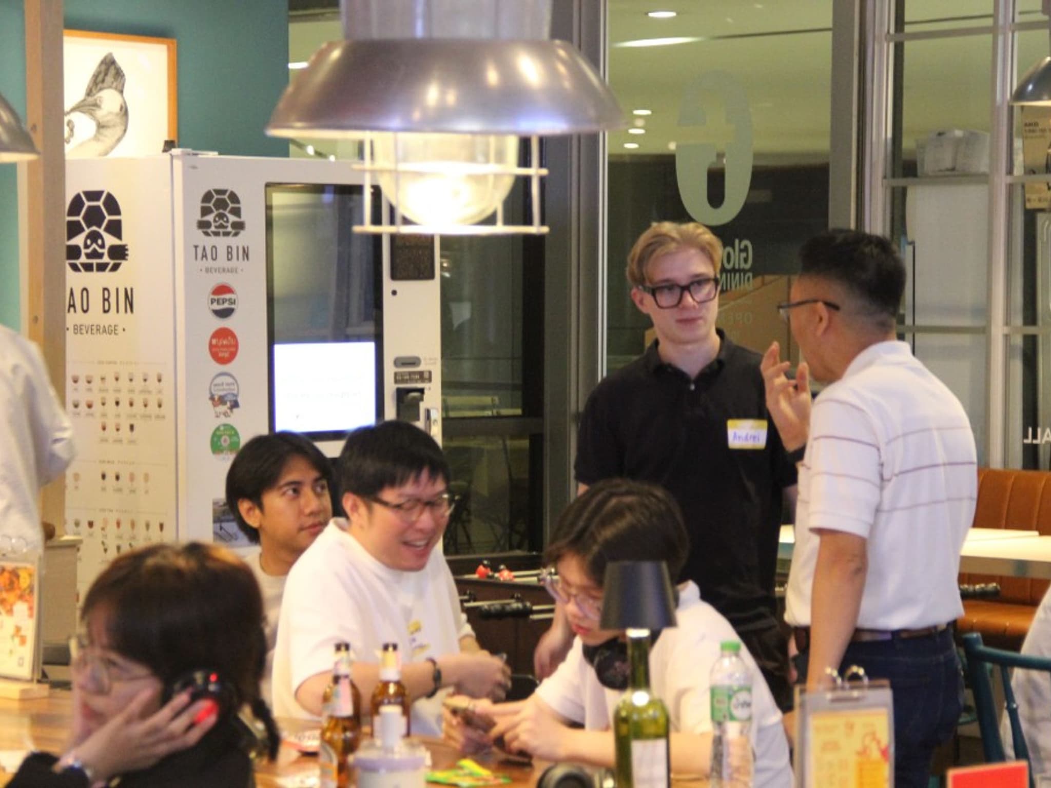 Head of Marketing Andrei Covalescu in conversation with Dr. Narong Kongpiwatana of Thammasat Business School and Sam Dhanakorn of AI-Kid School at a cafe table during Fish and Friends Day