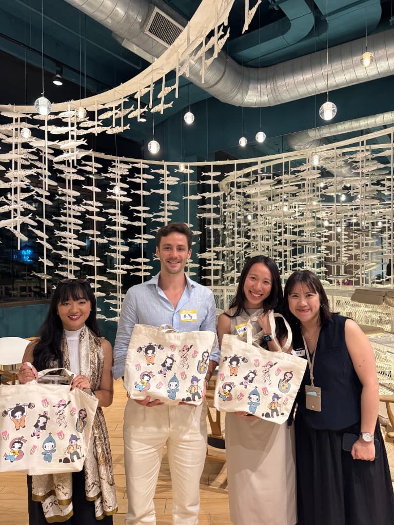 Priscilla Yeung and fellow speakers standing together under Glowfish's hanging fish installation, holding Fish and Friends tote bags