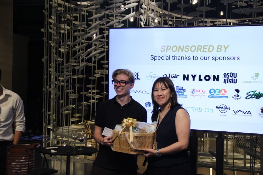 Priscilla Yeung holding a gift basket beside a sponsor screen at Fish and Friends Day