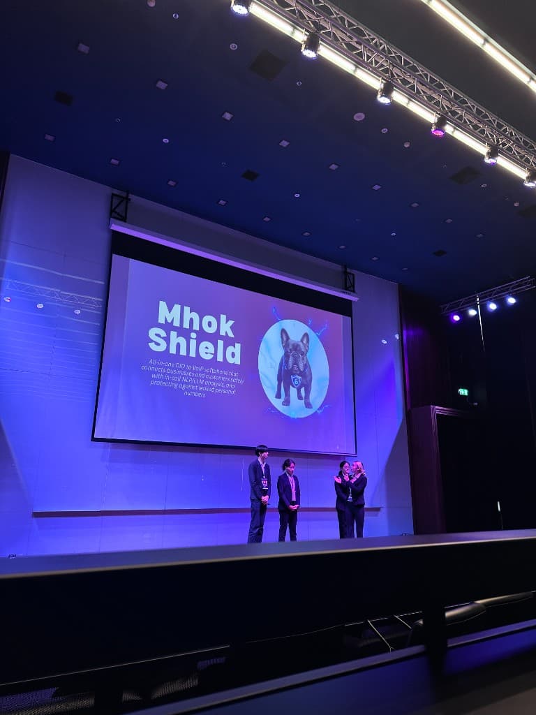 Three students on stage pitching Mhok Shield at UniHack 2026