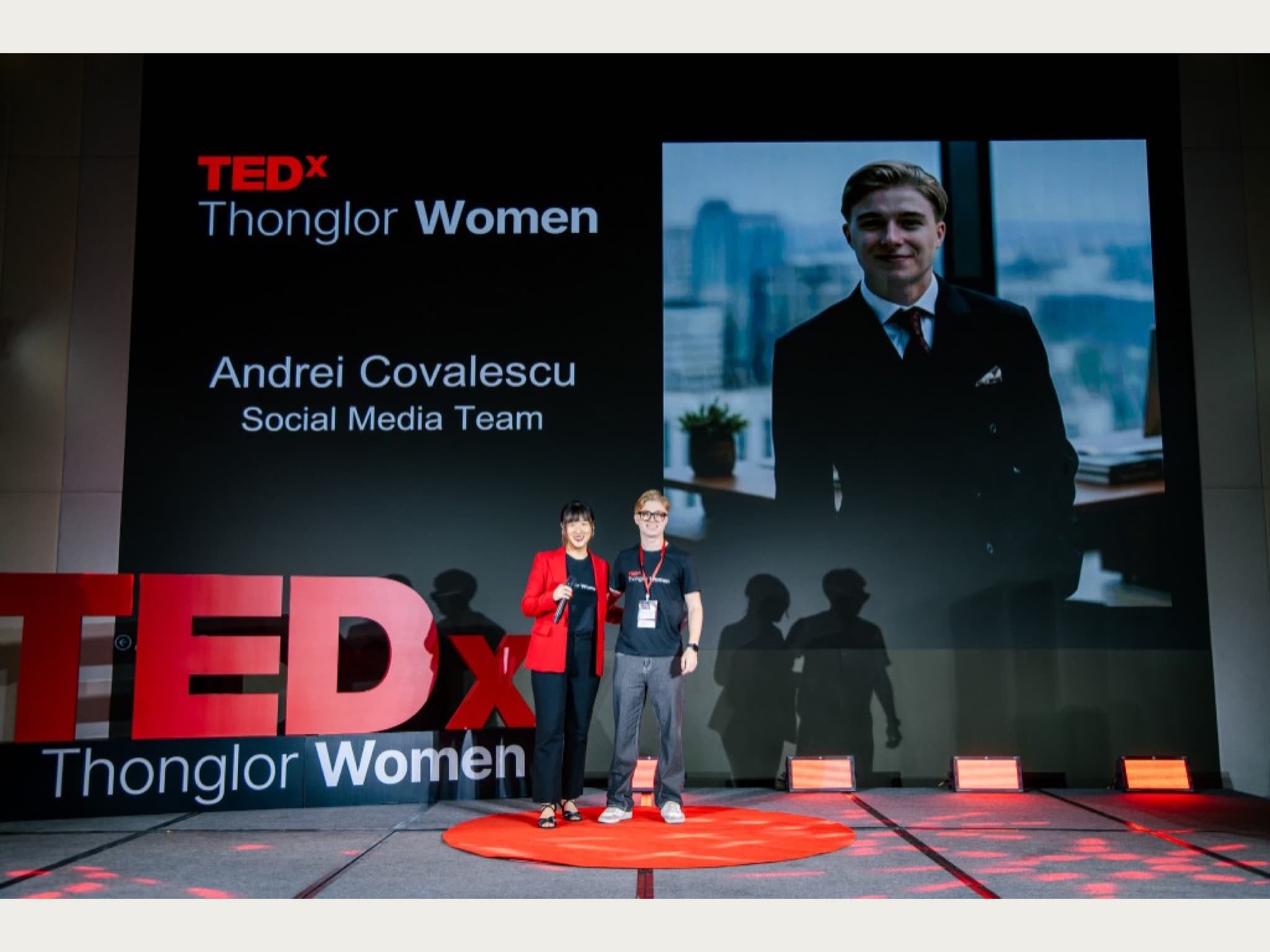 Andrei Covalescu on stage at TEDxThonglorWomen beside a host, with a screen showing his name and role on the social media team